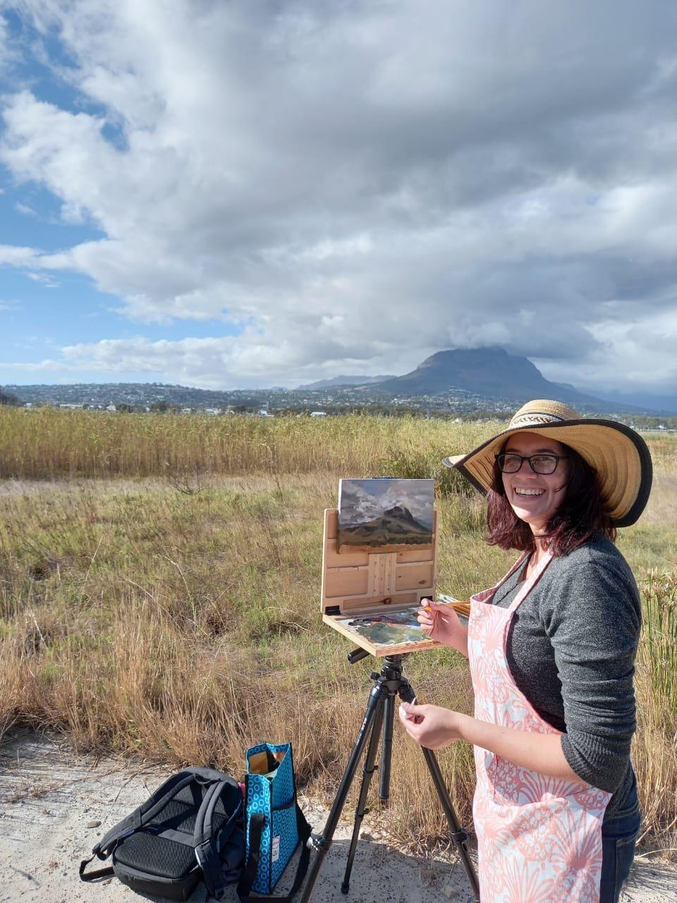 Tiana painting at a field easel in the veld with mountains behind