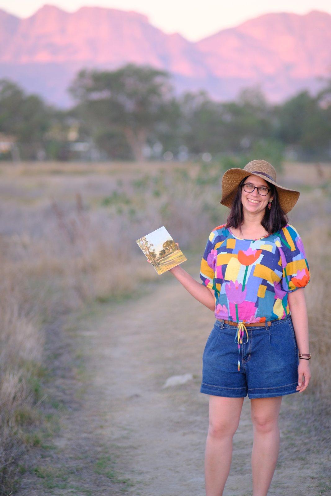 Tiana Goosen standing on a field path holding a small painting