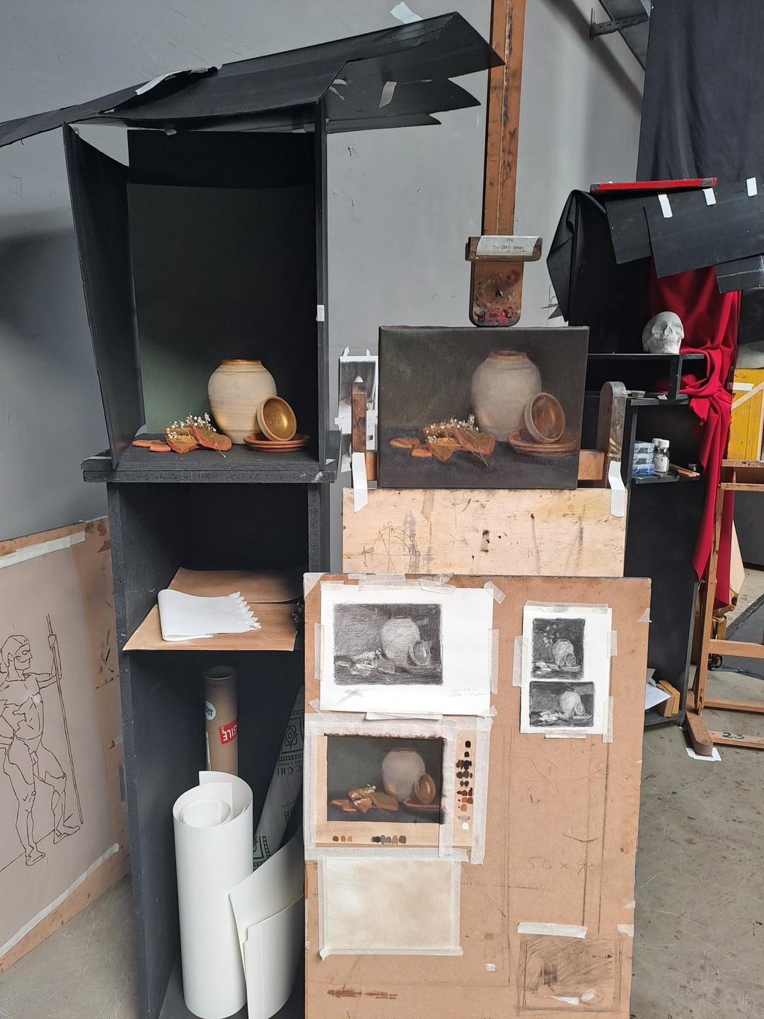 A still life set-up in a shadow box beside drawings and paintings in progress